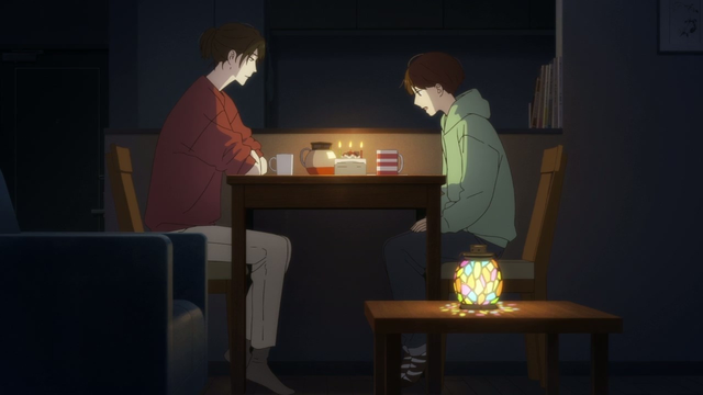 Anime screenshot: a young woman is sitting with a teenage girl at the table with a birthday cake, being lit with a light from a small multicoloured lamp