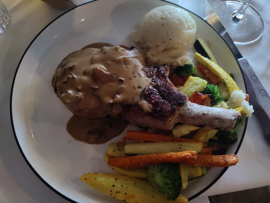 Pork chop with vegetables and mashed potatoes, with a mushroom sauce over top.